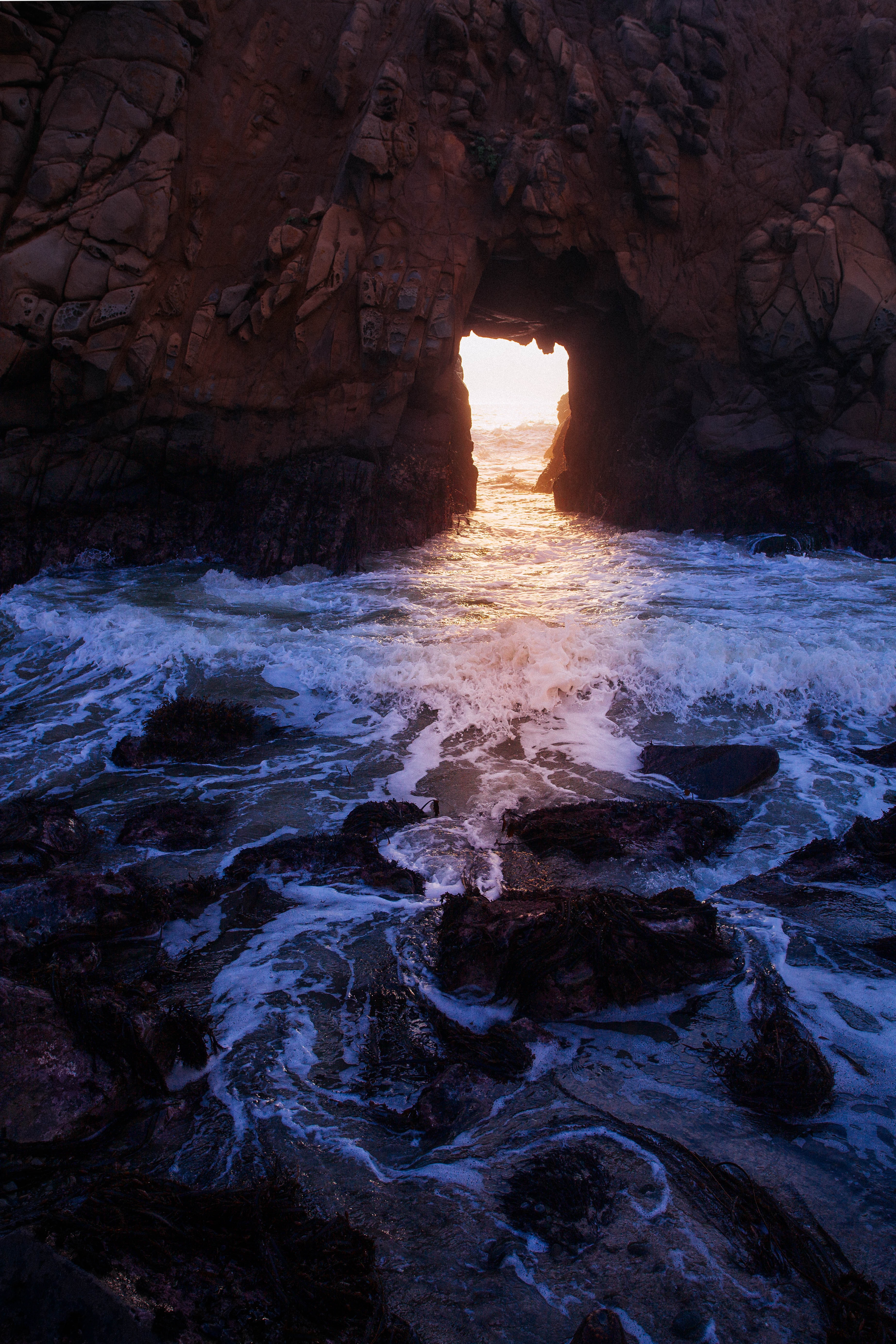 Golden light streaming through a natural ocean cave arch onto churning water